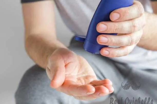 Sporty man holding a blue plastic tube and applying moisturizing cream on his hand. Cares about clean and soft hands